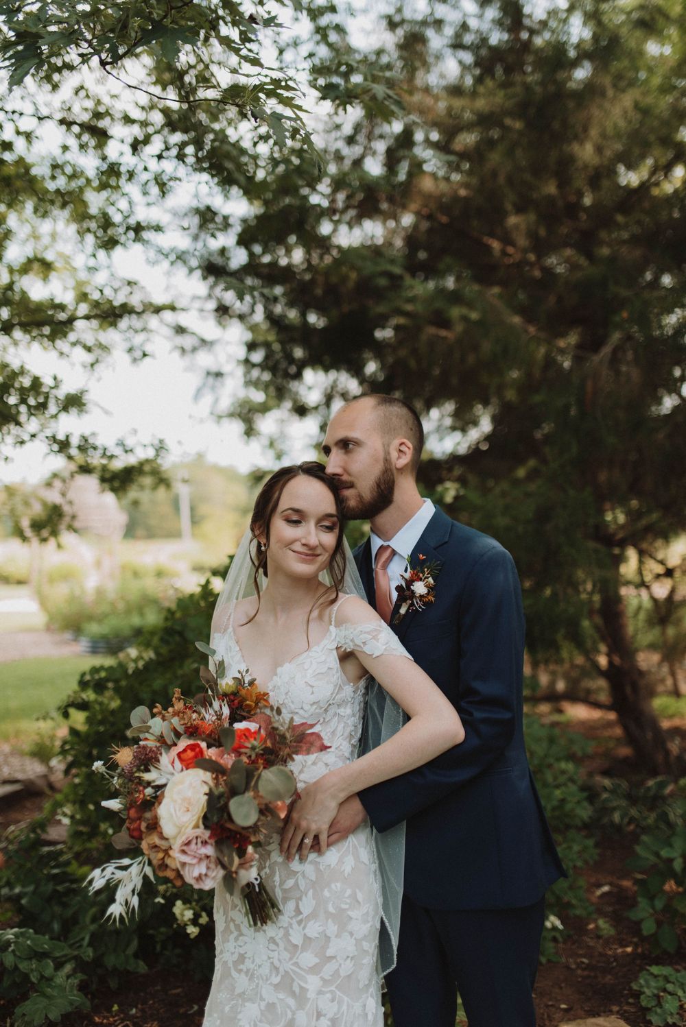 A romantic outdoor wedding photo with a couple embracing in a garden setting, featuring a beautiful autumn bouquet.