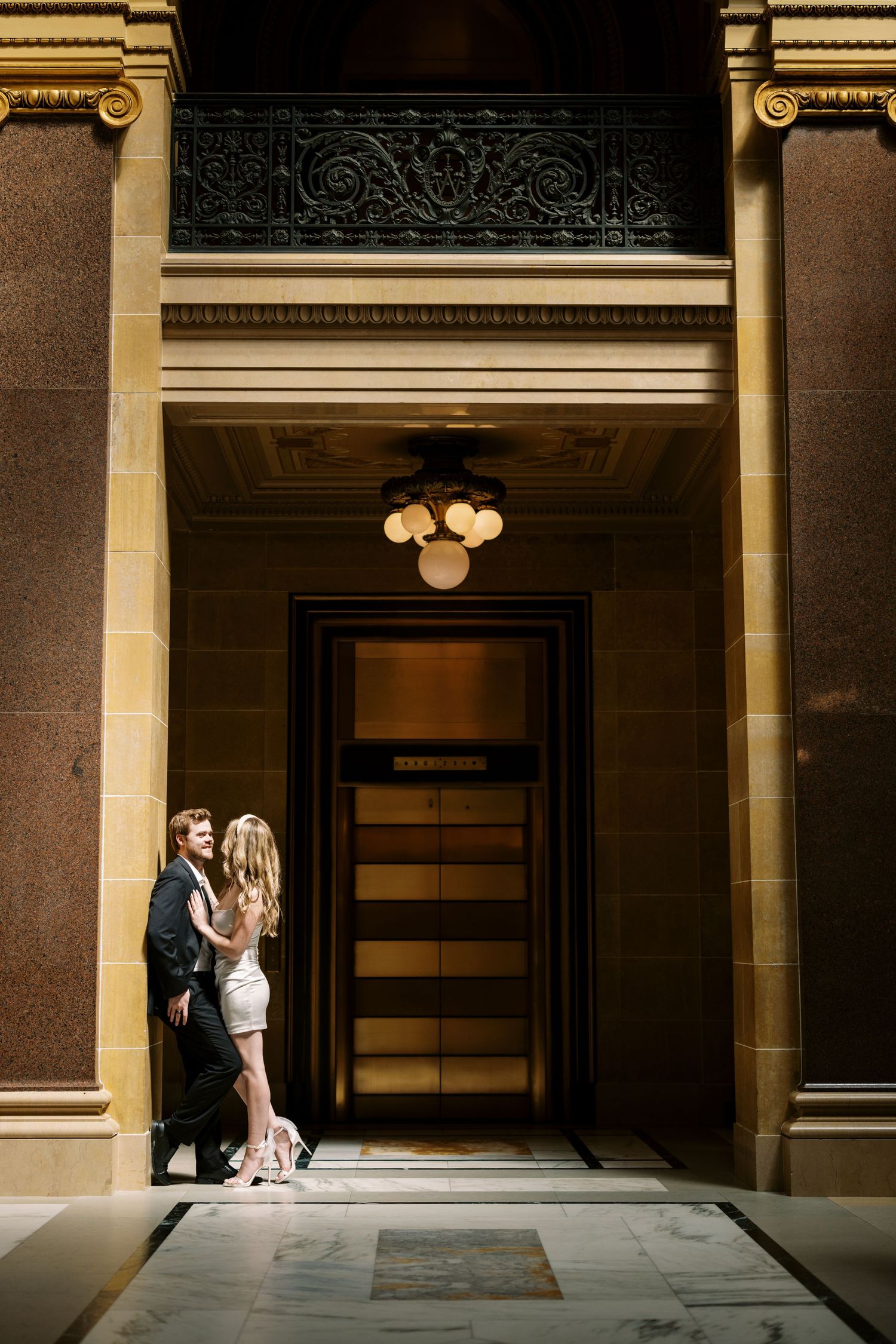 A couple shares an intimate moment in an elegant doorway with ornate architectural details and vintage lighting.