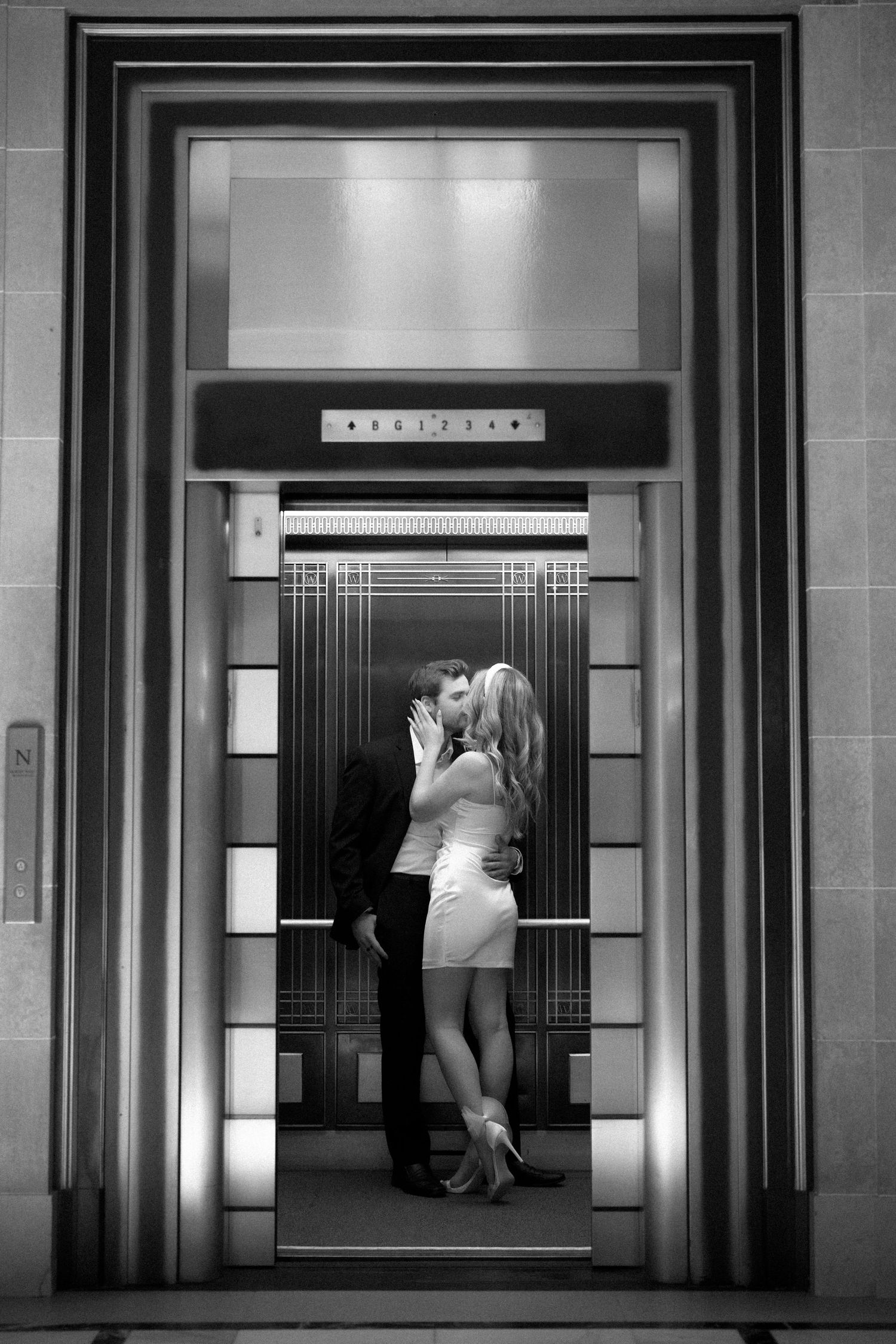 Black and white photograph of a romantic moment captured in an art deco elevator with geometric details and lighting.