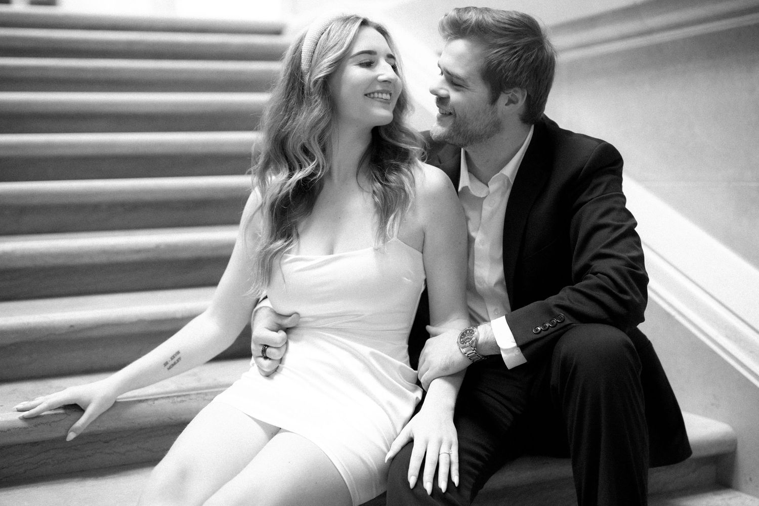 A joyful bride and groom share a candid moment together while seated on elegant marble stairs.