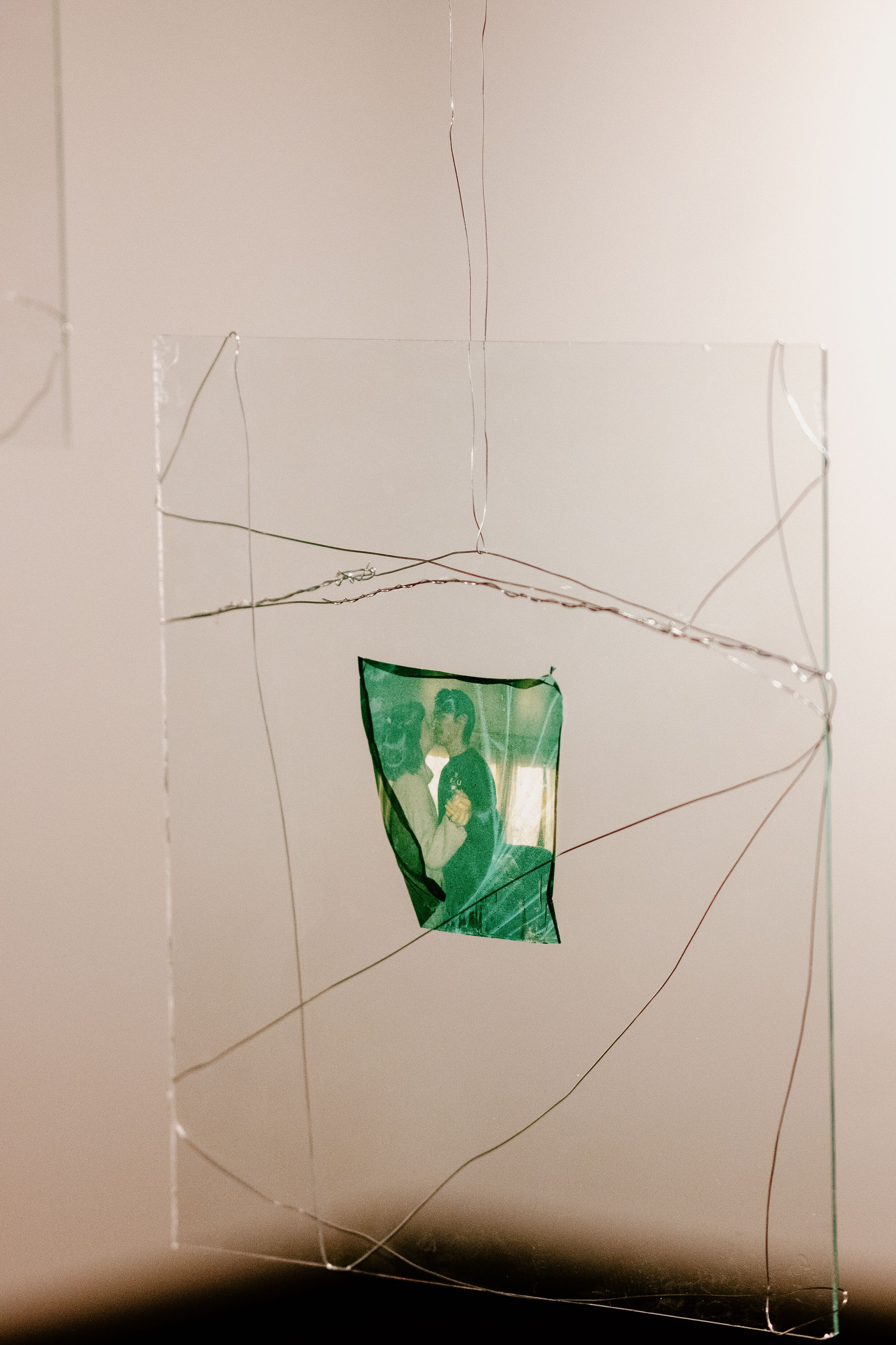 Abstract art installation with green fragments suspended in clear geometric frames against white wall.