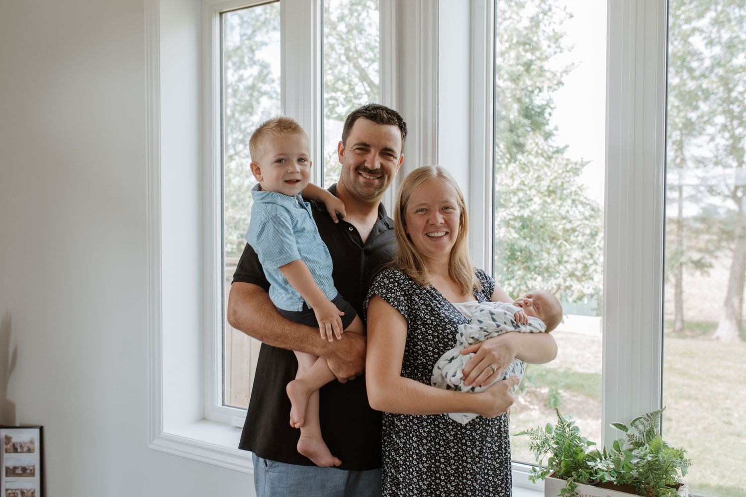 A happy family poses together near large windows in their bright modern home.