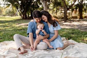 A loving family spends quality time together while sitting on a blanket in a sunny park setting.