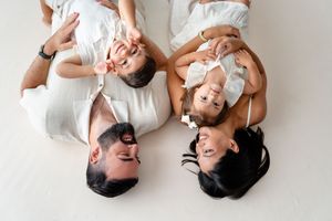 A portrait of a happy family lying on white bedding, smiling together while wearing white clothing.