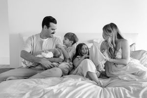 Family laughing and playing together on white bed sheets in sequence of black and white lifestyle photos.