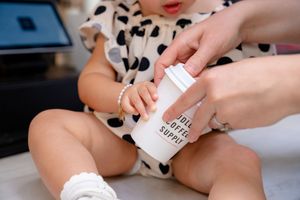Baby wearing a polka dot dress gets a diaper cream applied by adult hands with a pink nail polish.