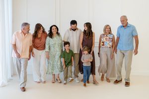Multi-generational family of eight smiling and walking together in a bright white studio during a professional portrait session.
