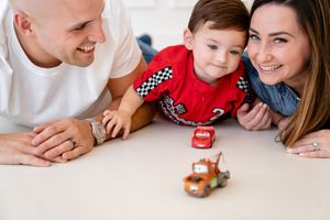Small toy cars are being played with on a white surface as hands lean in from the sides to interact.