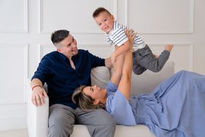 A parent and child play together on a white couch in a bright living room setting.