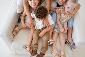 Four pairs of feet wearing comfortable summer sandals shown close up while sitting together on white floor mat.