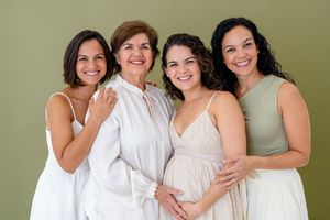 A group of women in coordinating white and beige outfits smile together in a casual photo session against a neutral backdrop.