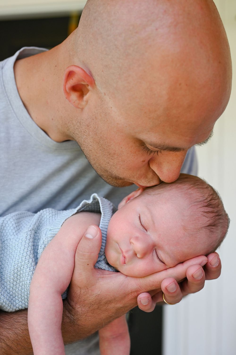 A tender moment between an adult and sleeping newborn baby cradled gently in protective hands.