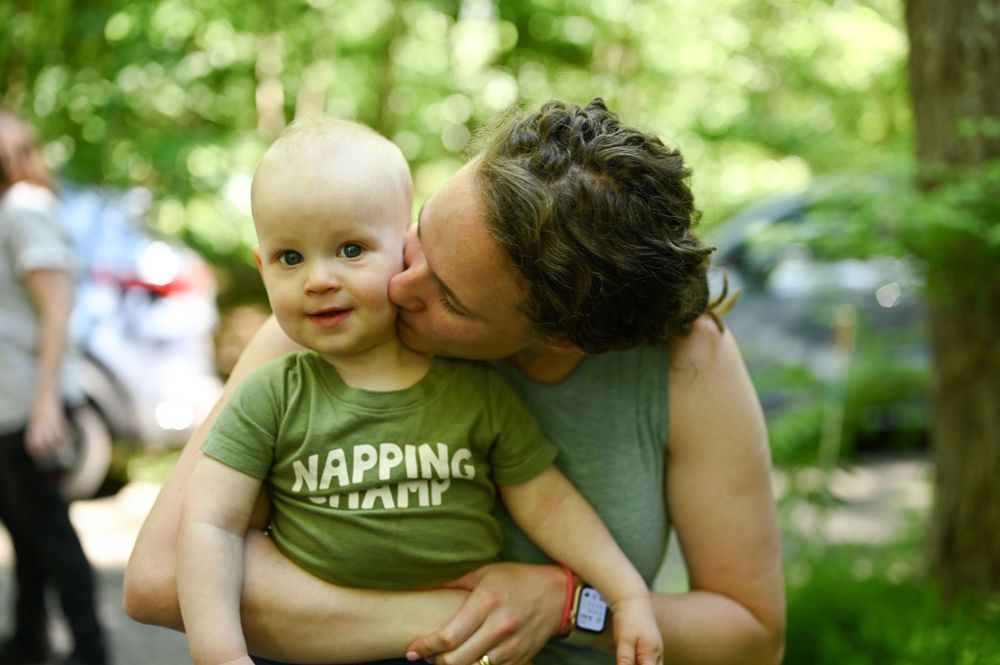 A tender moment between parent and baby outdoors with greenery in the background.