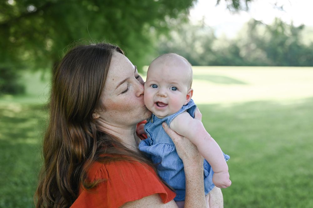 A joyful outdoor moment between parent and baby in casual attire on a sunny day in a grassy park setting.