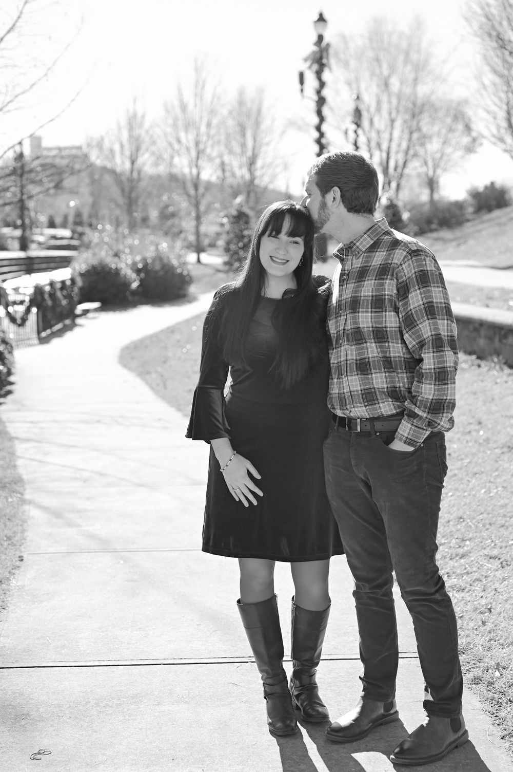 A stylish couple poses together on a scenic park pathway in winter.