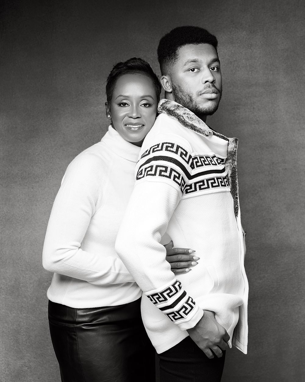 Black and white portrait of two people in matching Greek key patterned sweaters posing back to back.