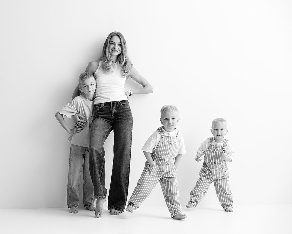 Black and white photo of a mom posing with her three young children against a white background.
