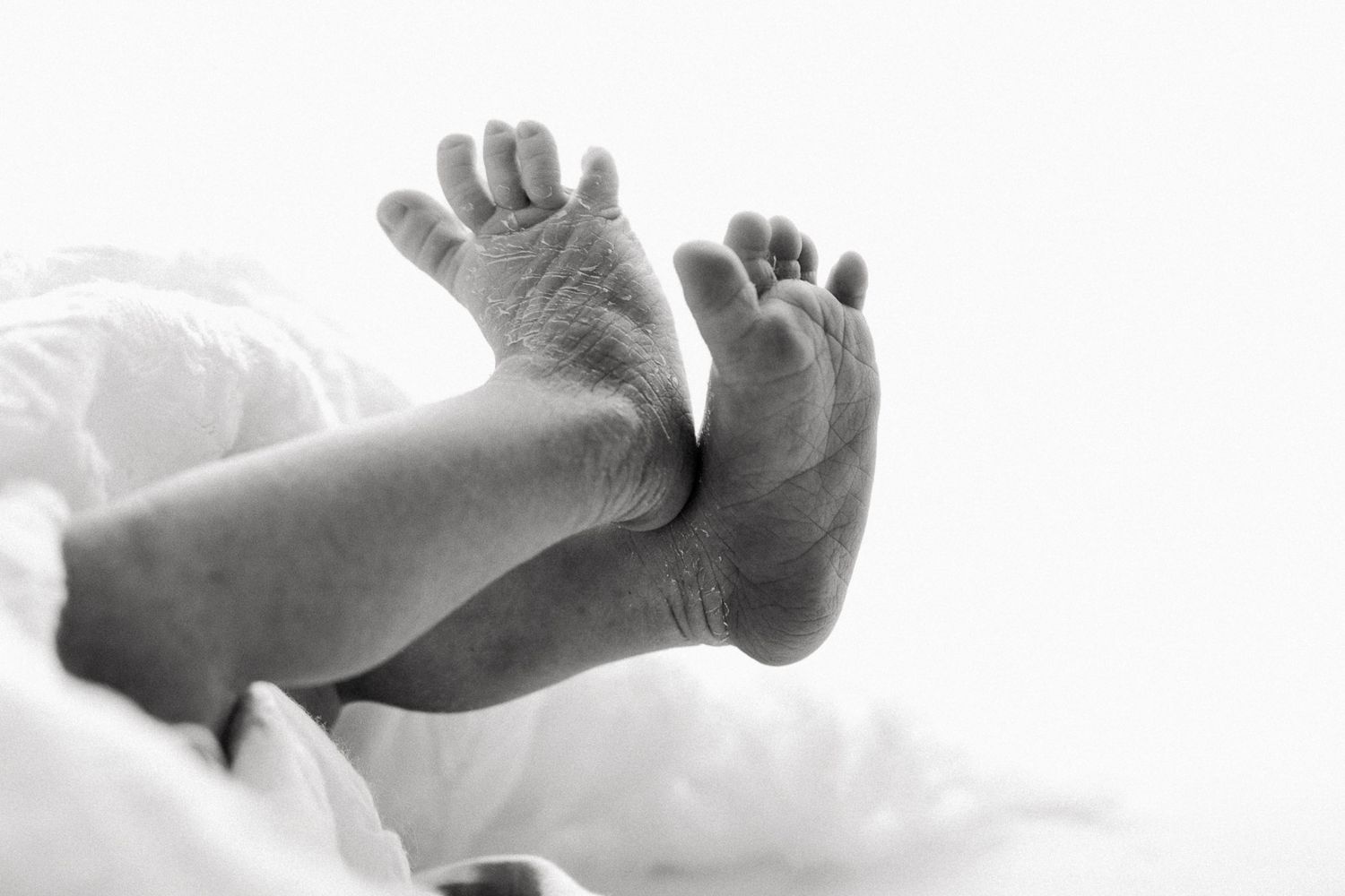 Black and white close-up photo of tiny baby feet against soft white bedding.