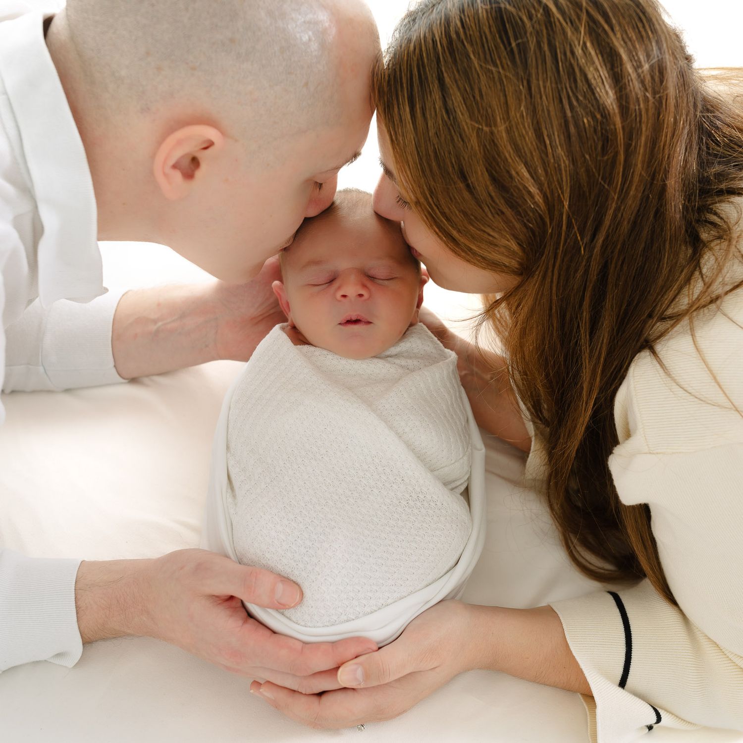 Tender moment between parent and baby in white bedding showing nurturing care and affection.