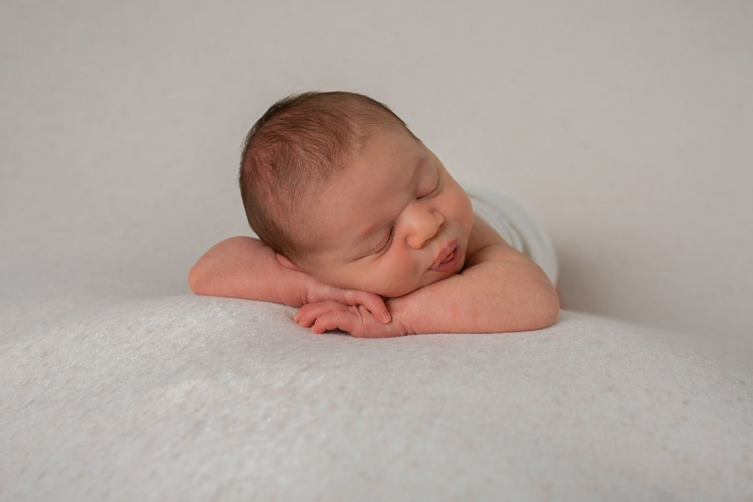 A sleeping newborn baby rests peacefully on soft white blankets in a minimalist studio portrait setting.