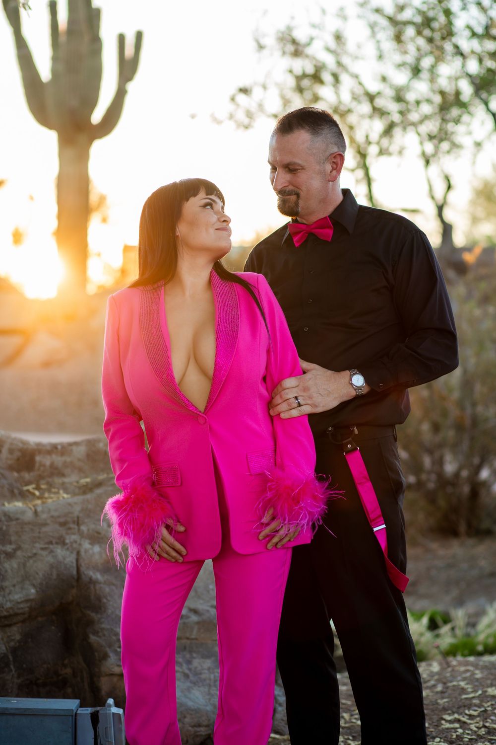 Couple in coordinating pink and black outfits posing at sunset in desert landscape.