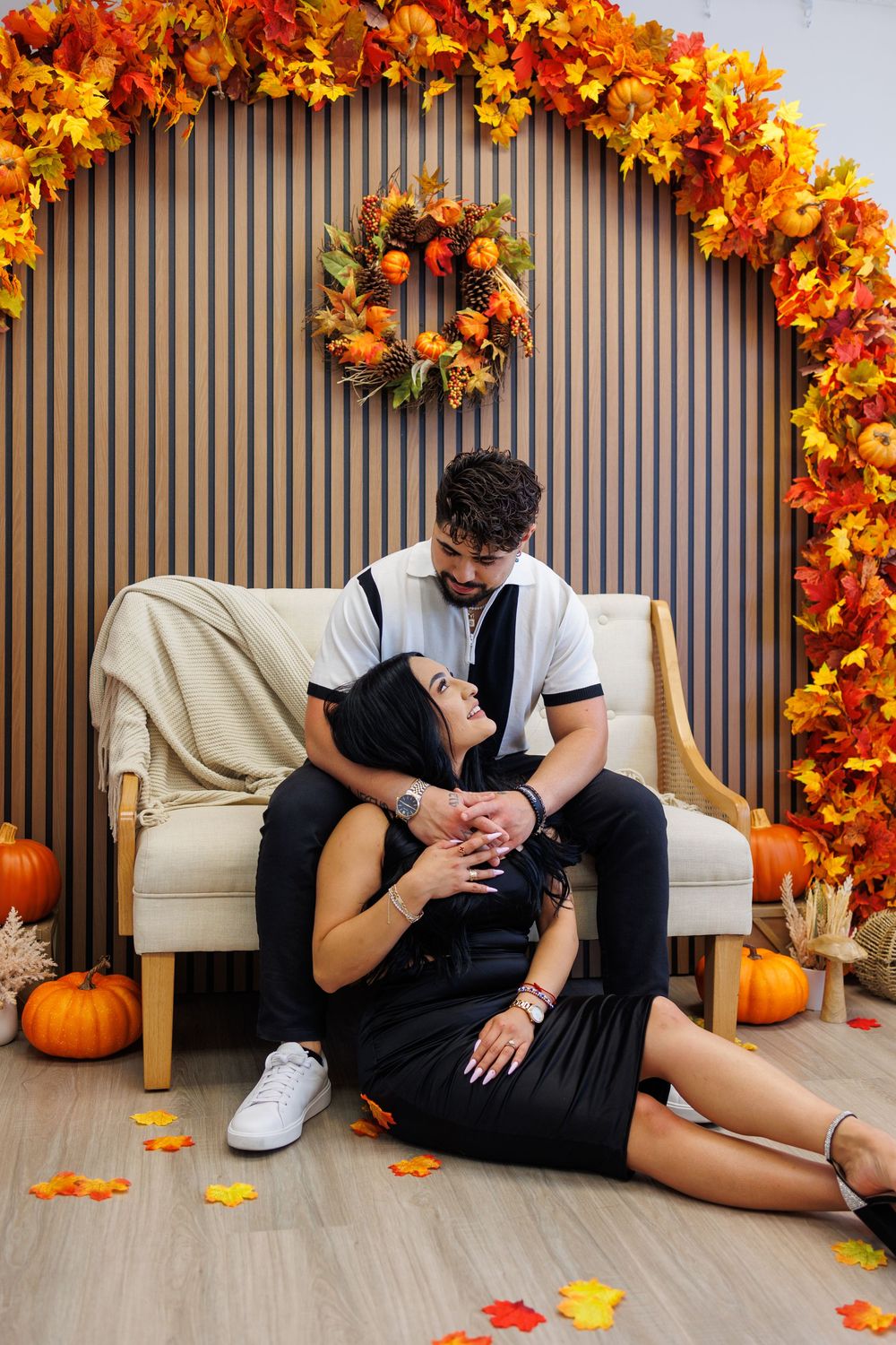 Couple posing in autumn-themed studio with colorful fall leaves and pumpkin decorations.