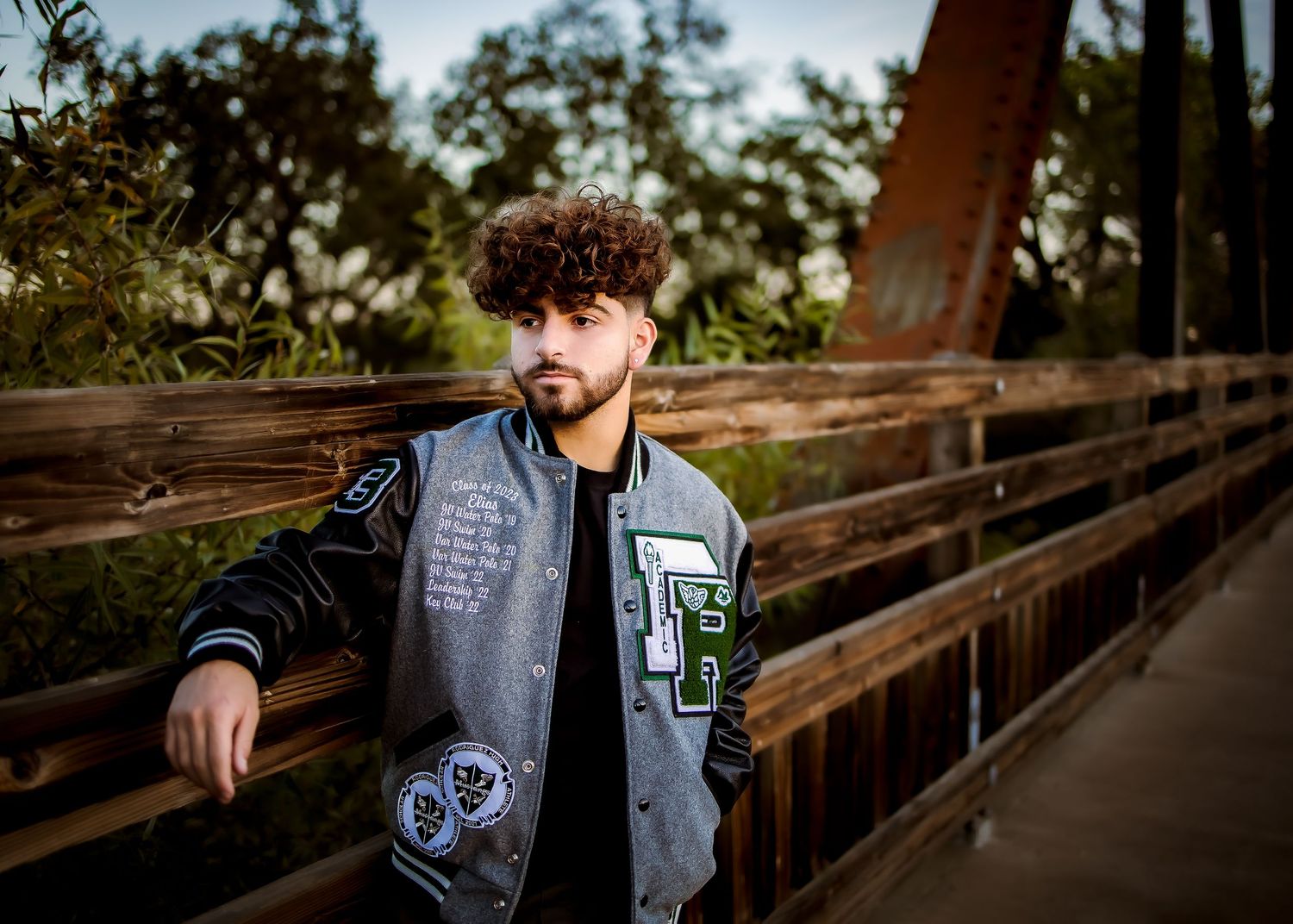 Senior portrait of boy standing on bridge wearing his letterman jacket in Winters, CA