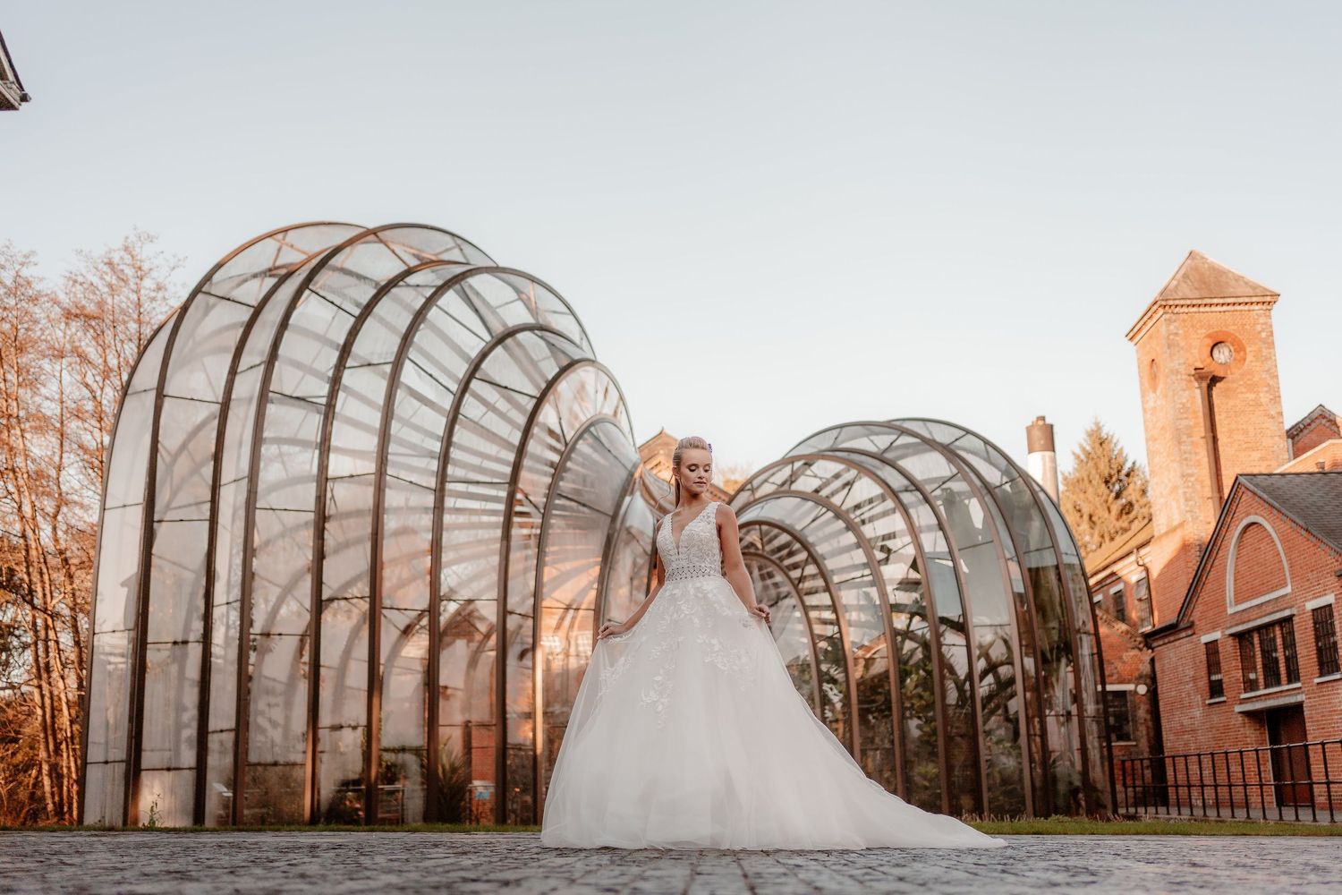 Bride in a white wedding dress stands in front of the Bombay Sapphire Distillery Glasshouses which frame her like wings