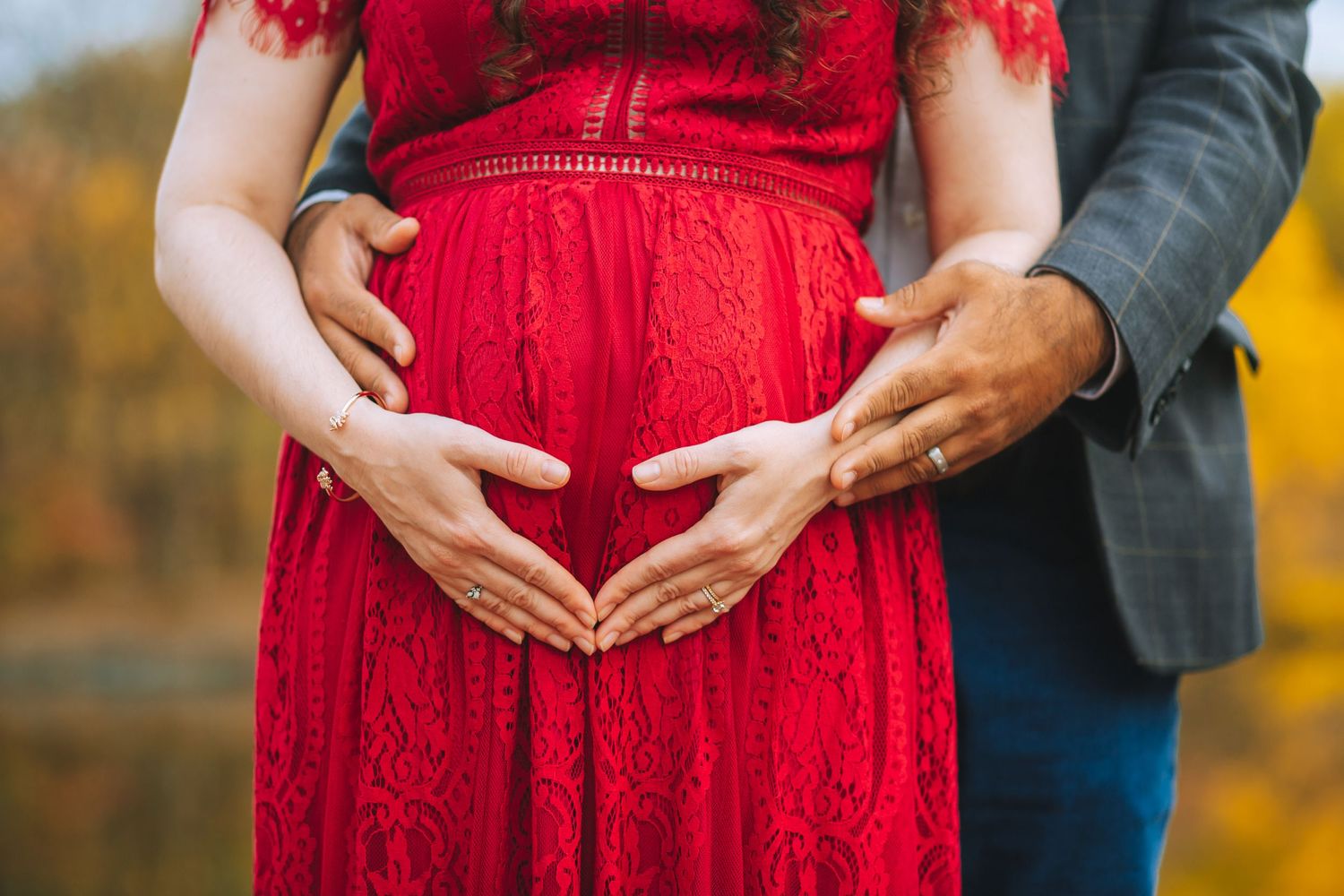 Close-up of hands forming a heart shape on a red maternity dress.