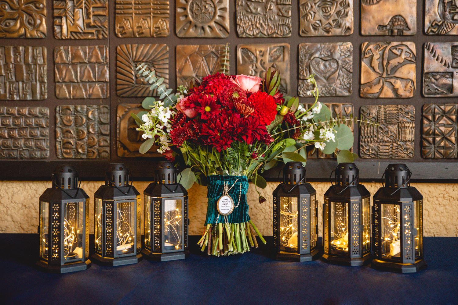 Wedding decor featuring black lanterns and a vibrant red bouquet against a decorative tiled wall.