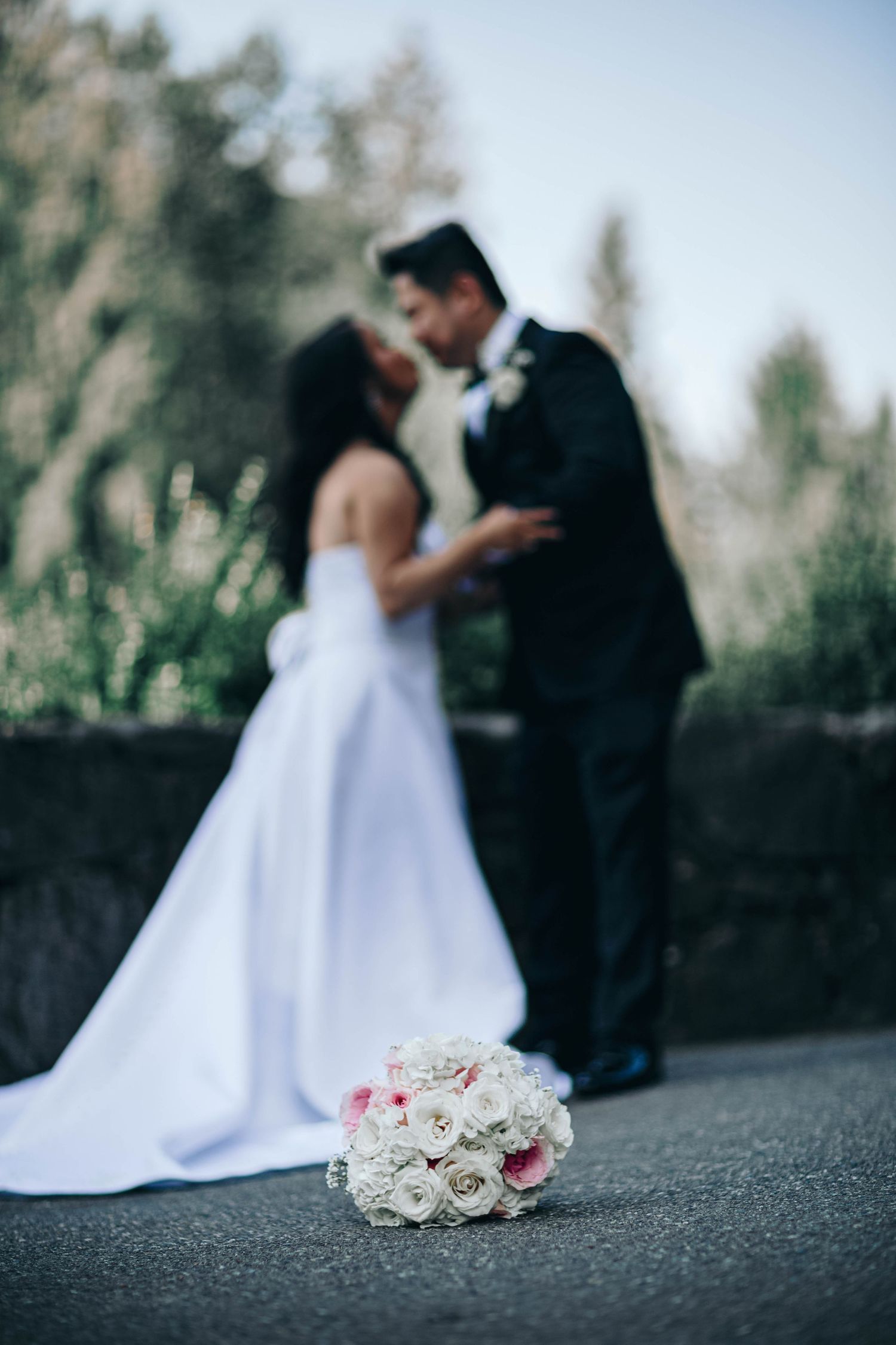 A wedding bouquet of white and pink roses in focus with newlyweds blurred in background.