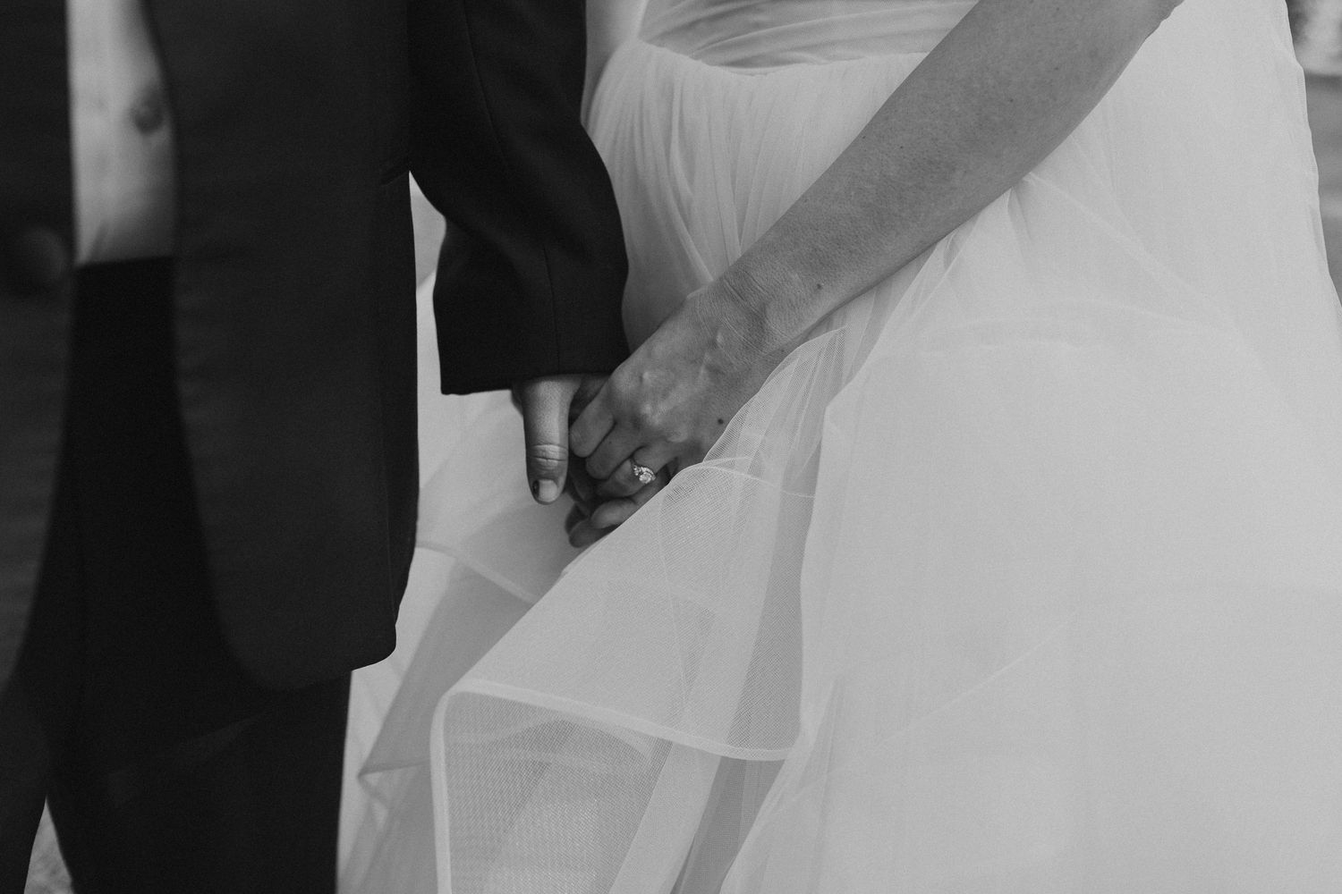 Black and white close-up of couple holding hands during a wedding ceremony.