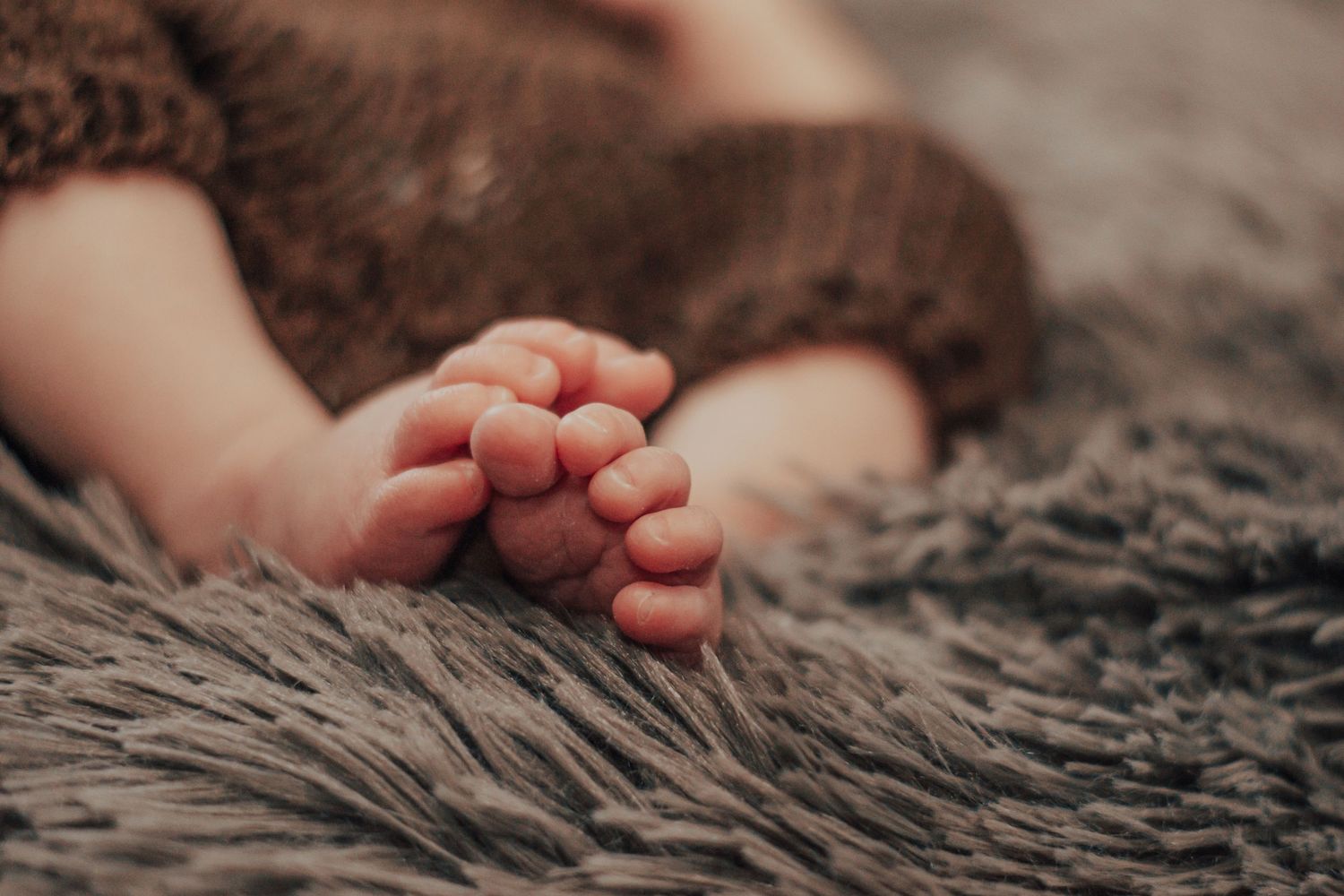 Close-up of tiny baby feet against textured gray blanket in soft lighting.