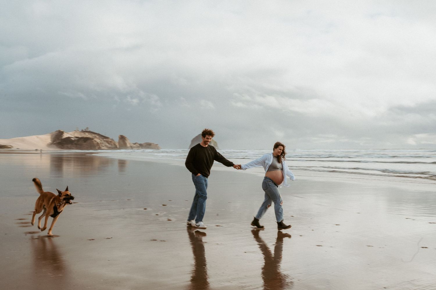 Playful couple runs along a misty beach with their dog.