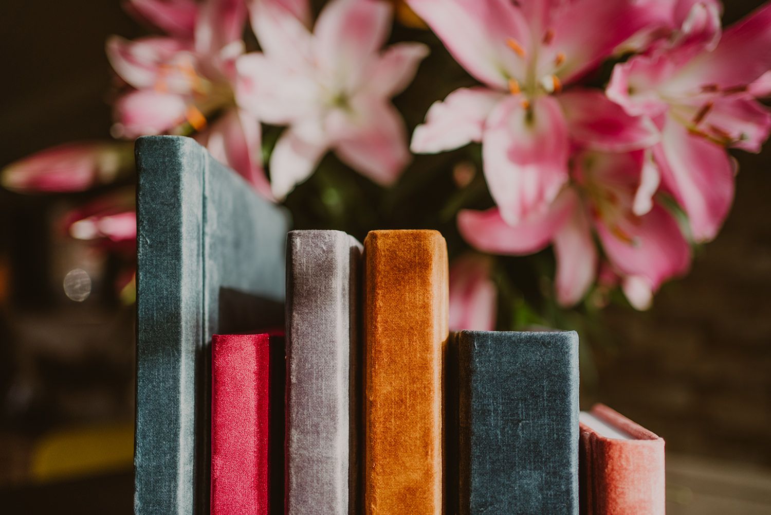 Vintage books arranged in colorful stack with pink flowers in background.