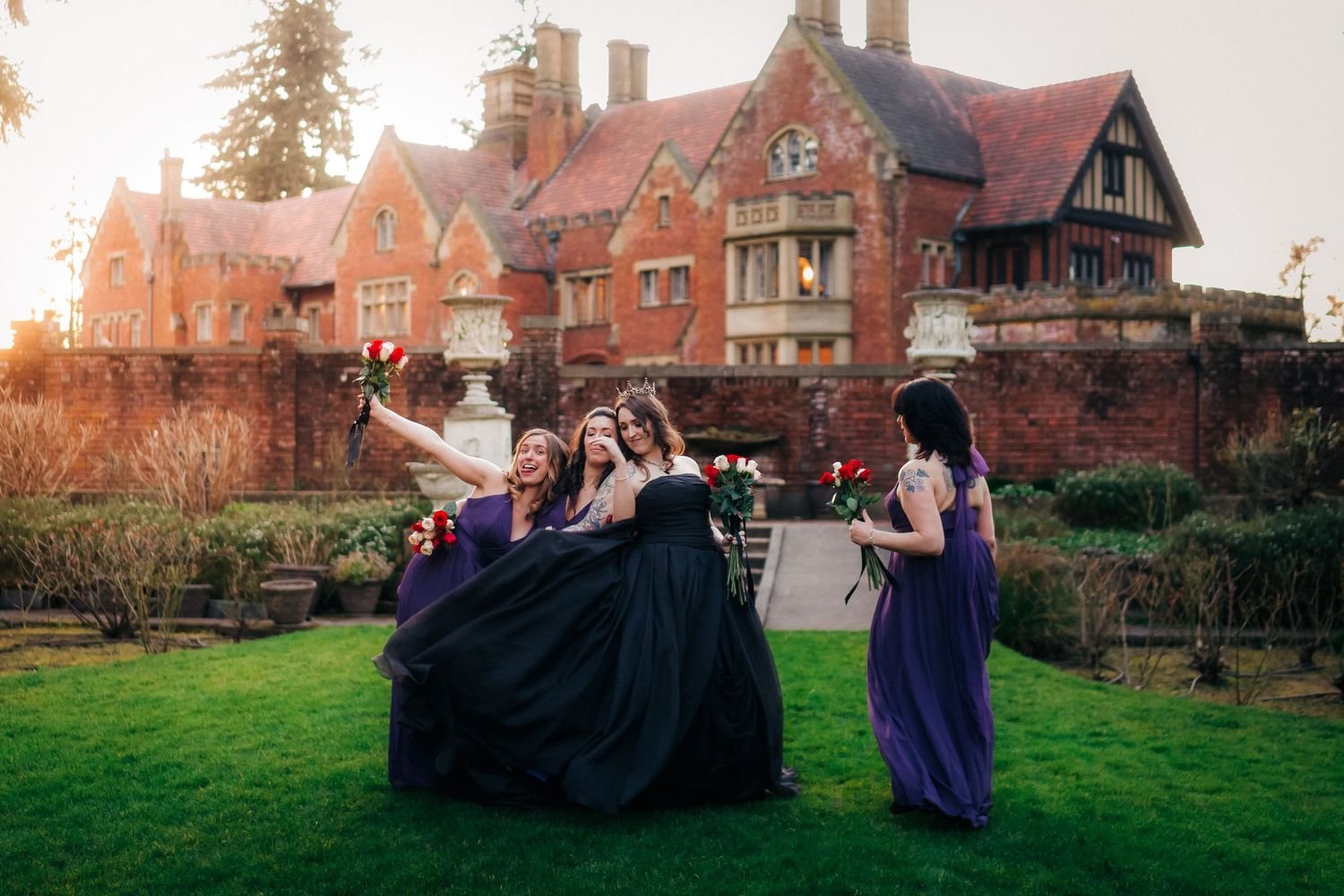 Group celebrating on lawn of historic Tudor-style mansion at sunset.