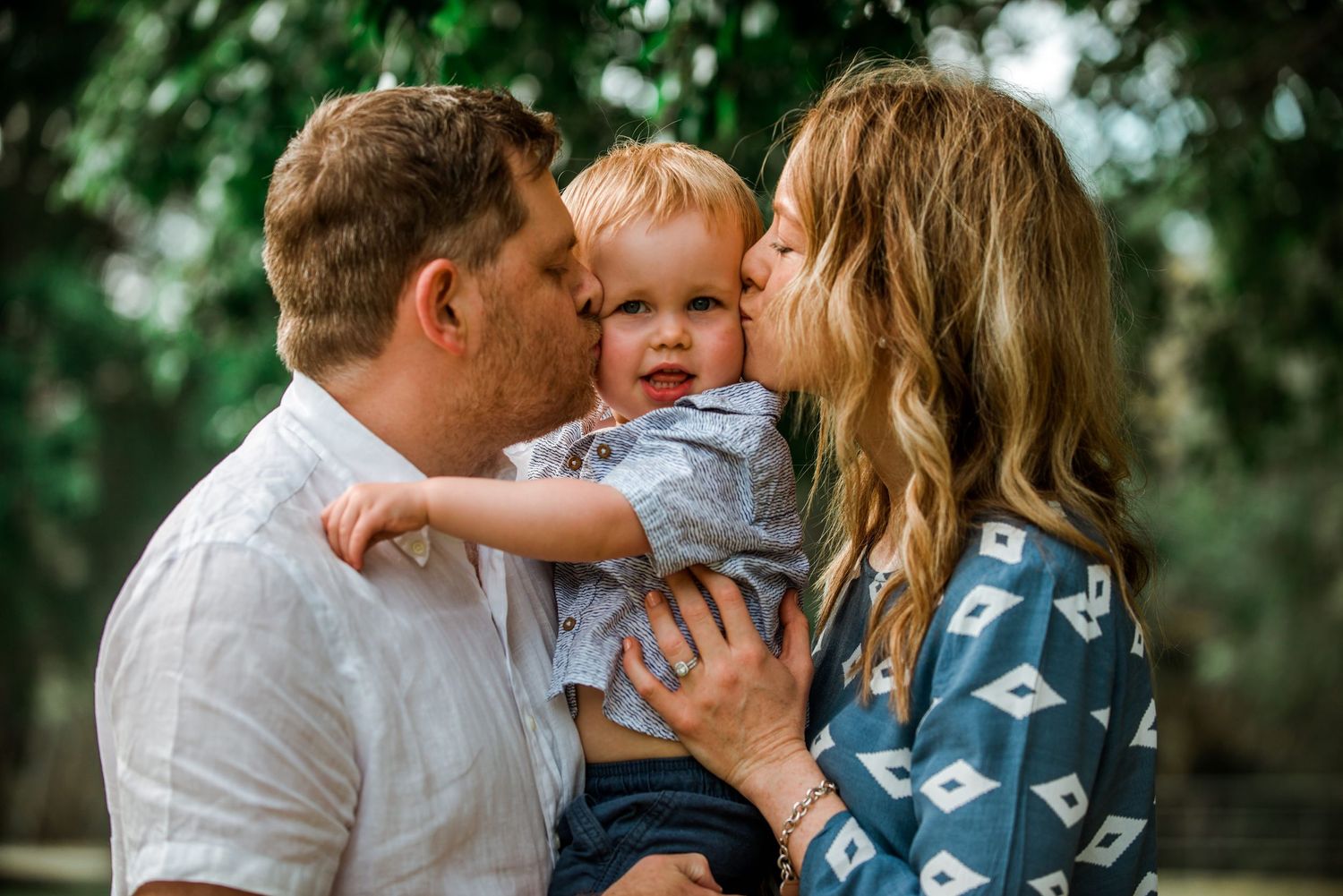 Family sharing tender moment outdoors with young child between parents.