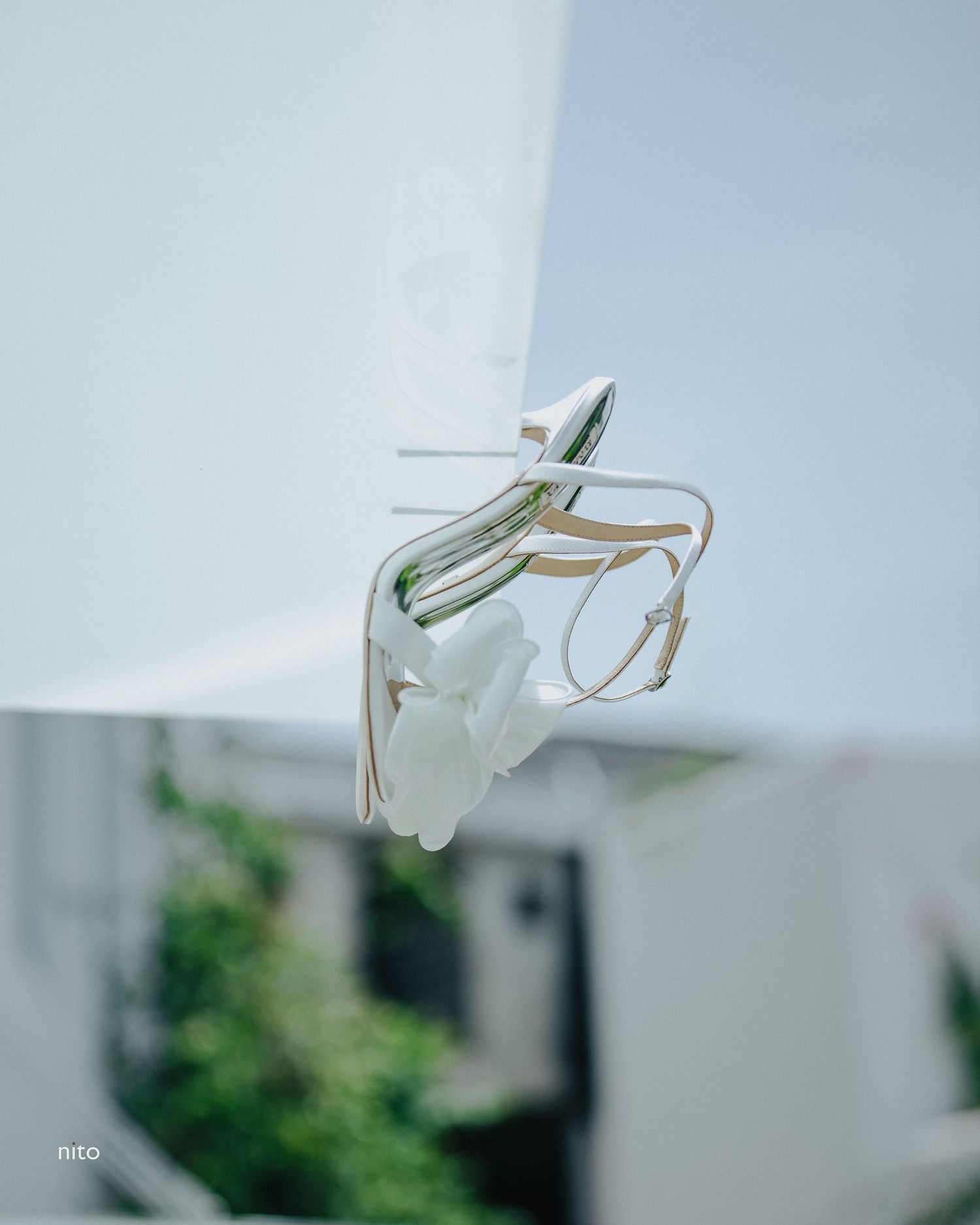 White strappy bridal sandals floating against minimalist white wall background.