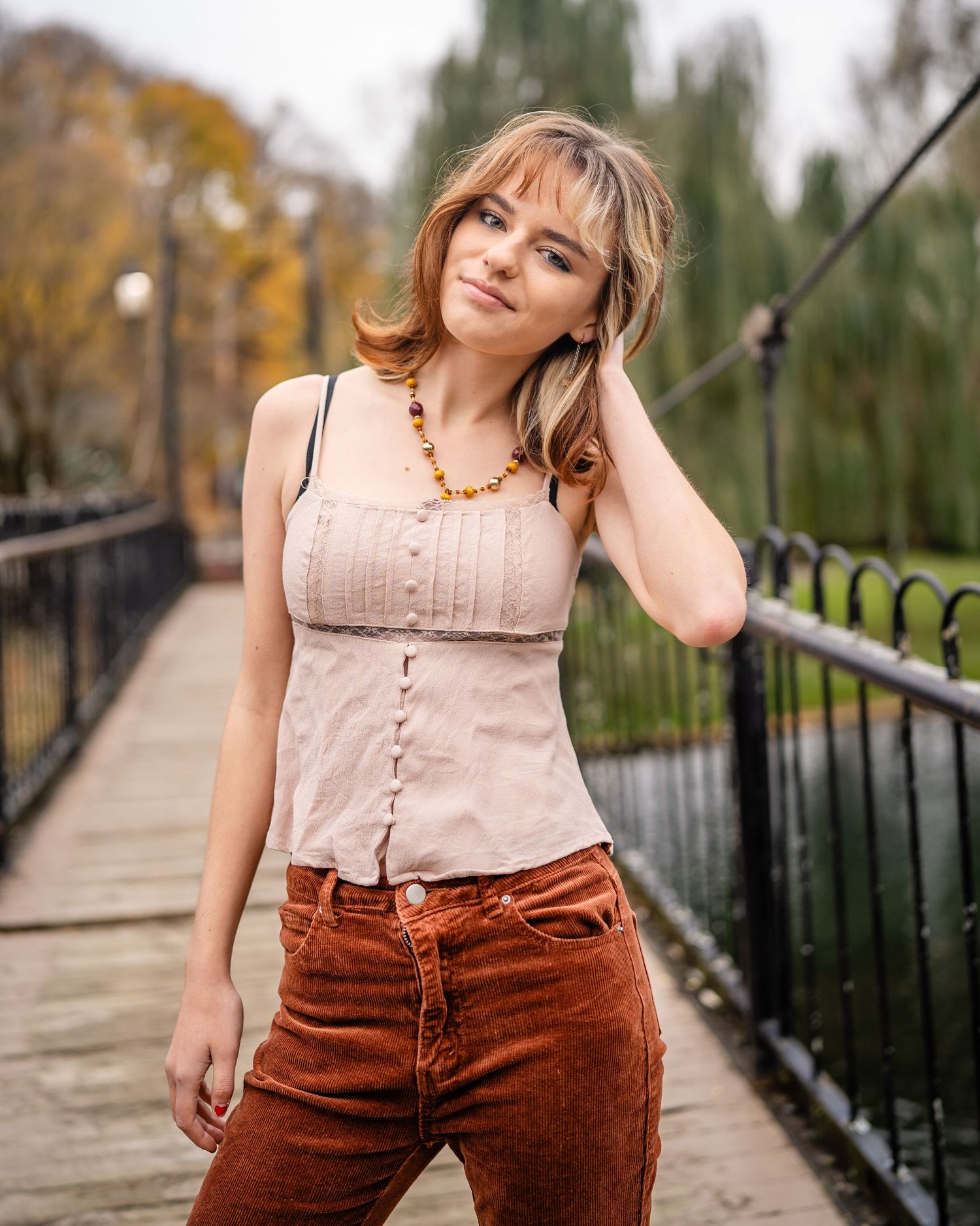 Portrait on wooden bridge with autumn foliage in background.