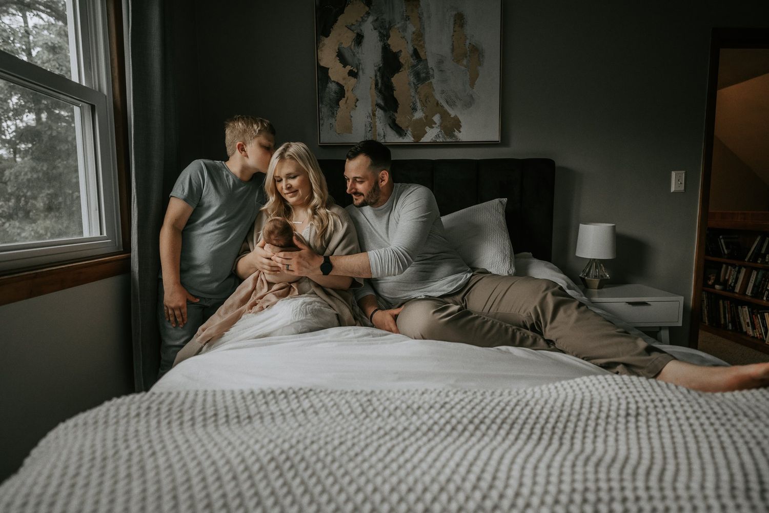 A cozy lifestyle scene of a family relaxing together on a bed in a dimly lit bedroom.