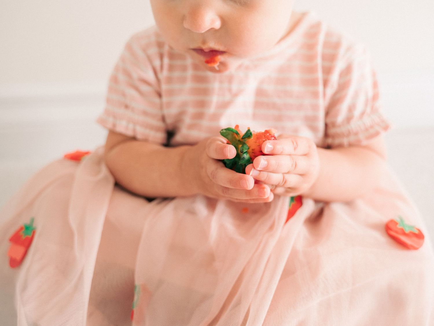 Someone in a pink striped dress holding a fresh strawberry.
