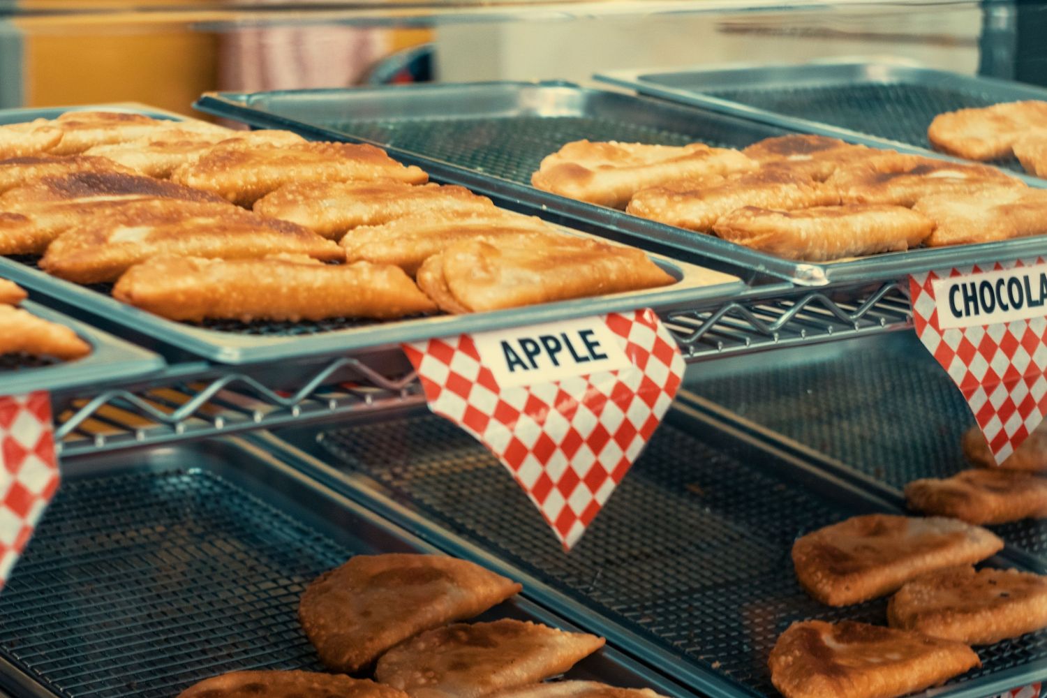 Fresh apple and chocolate fried pies displayed on bakery rack with red checkered labels.