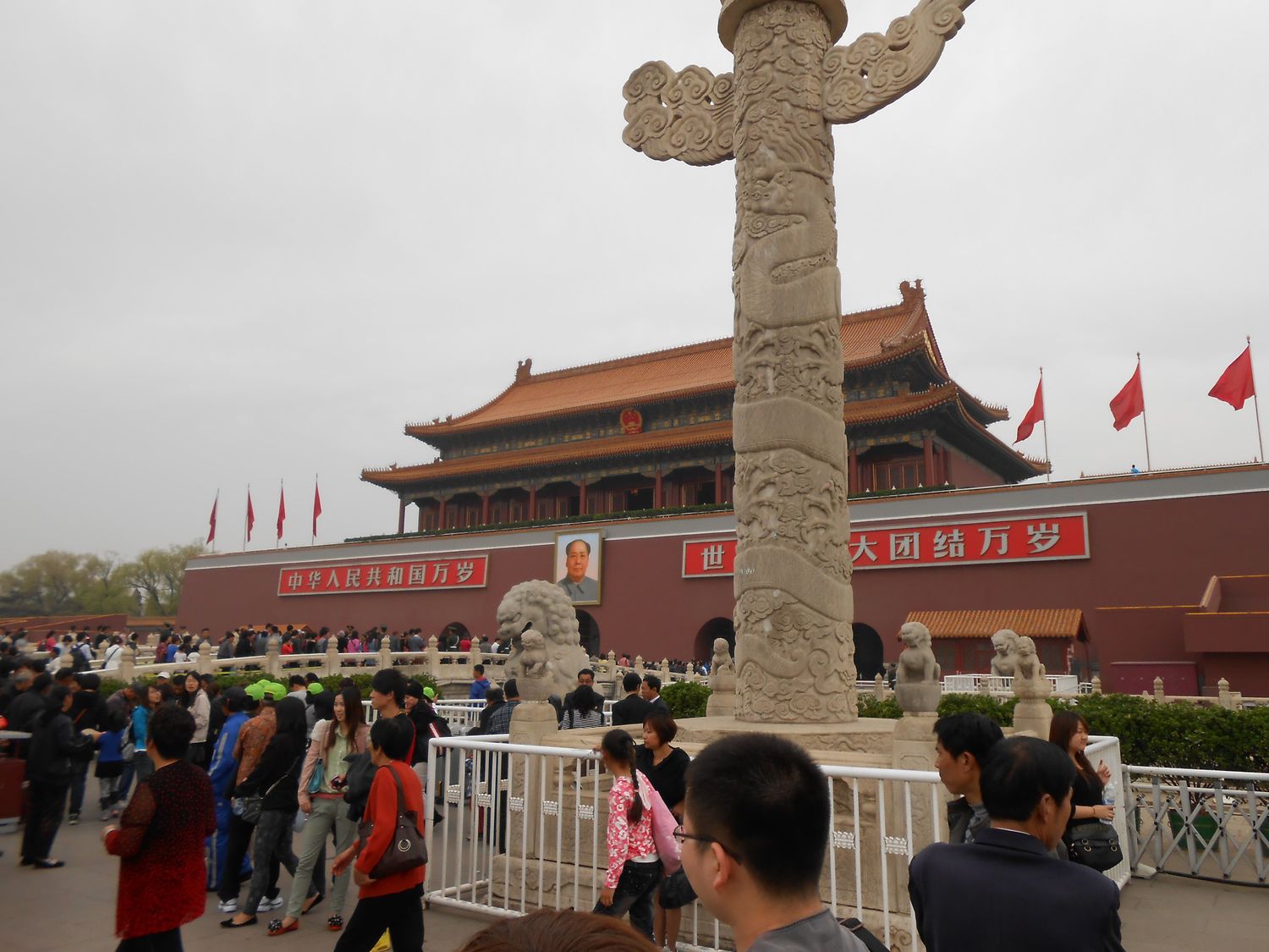Tourists visiting Tiananmen Square in Beijing, China, with ornate stone pillar in foreground.