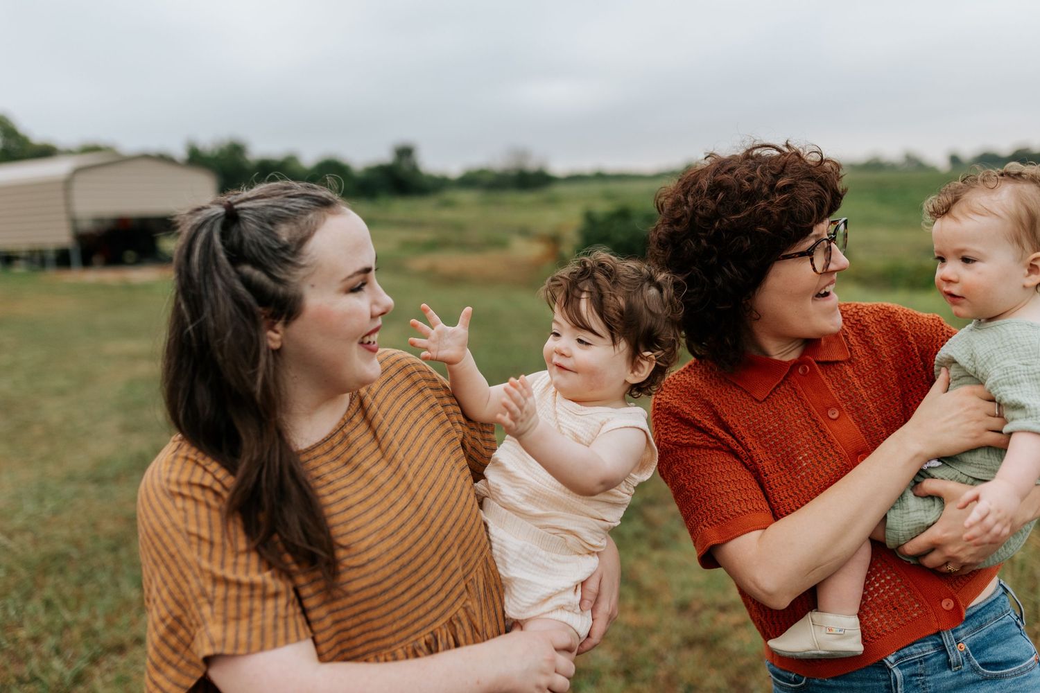 LGBTQ family portrait with two moms laughing as they hold their smiling twin babies in a field in Olathe, KS.