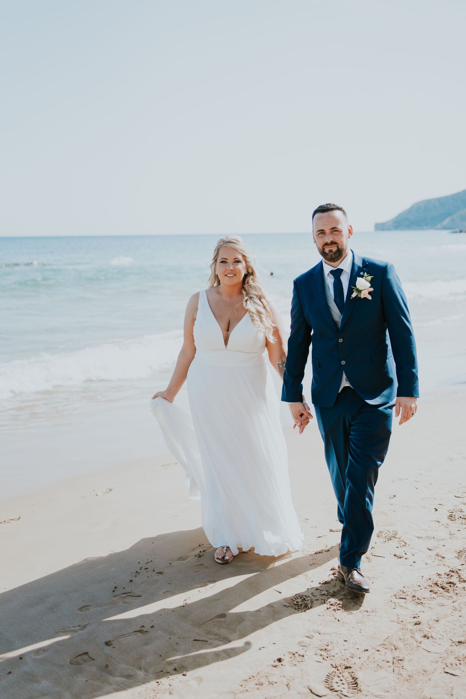 Couple walking on a beach with ocean and mountains in the background.