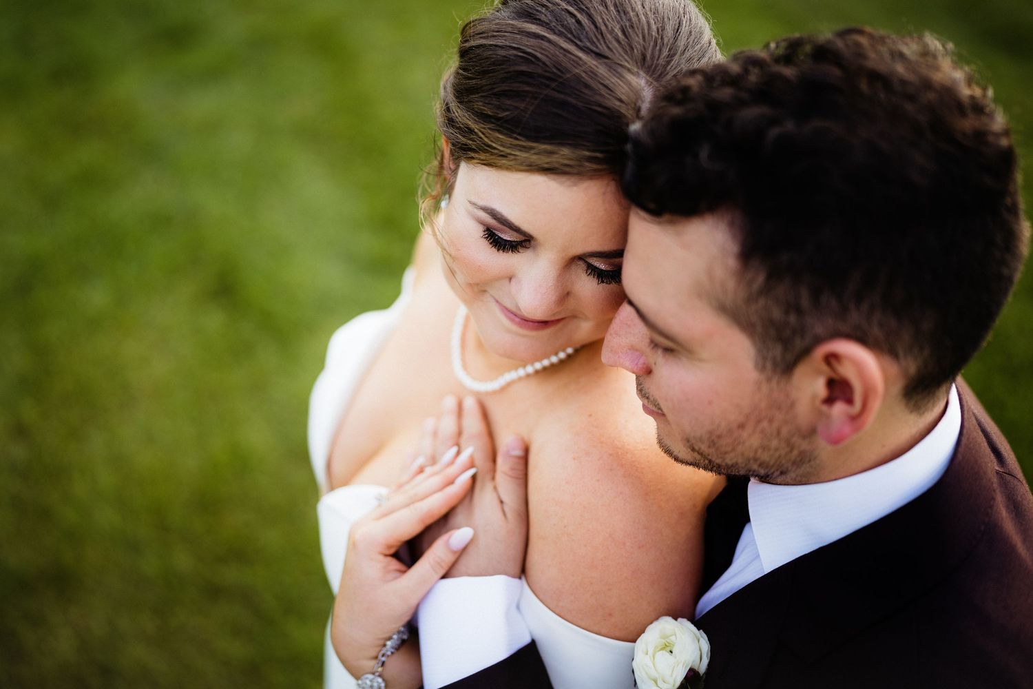 A romantic wedding portrait shows a tender moment between newlyweds in outdoor lighting.
