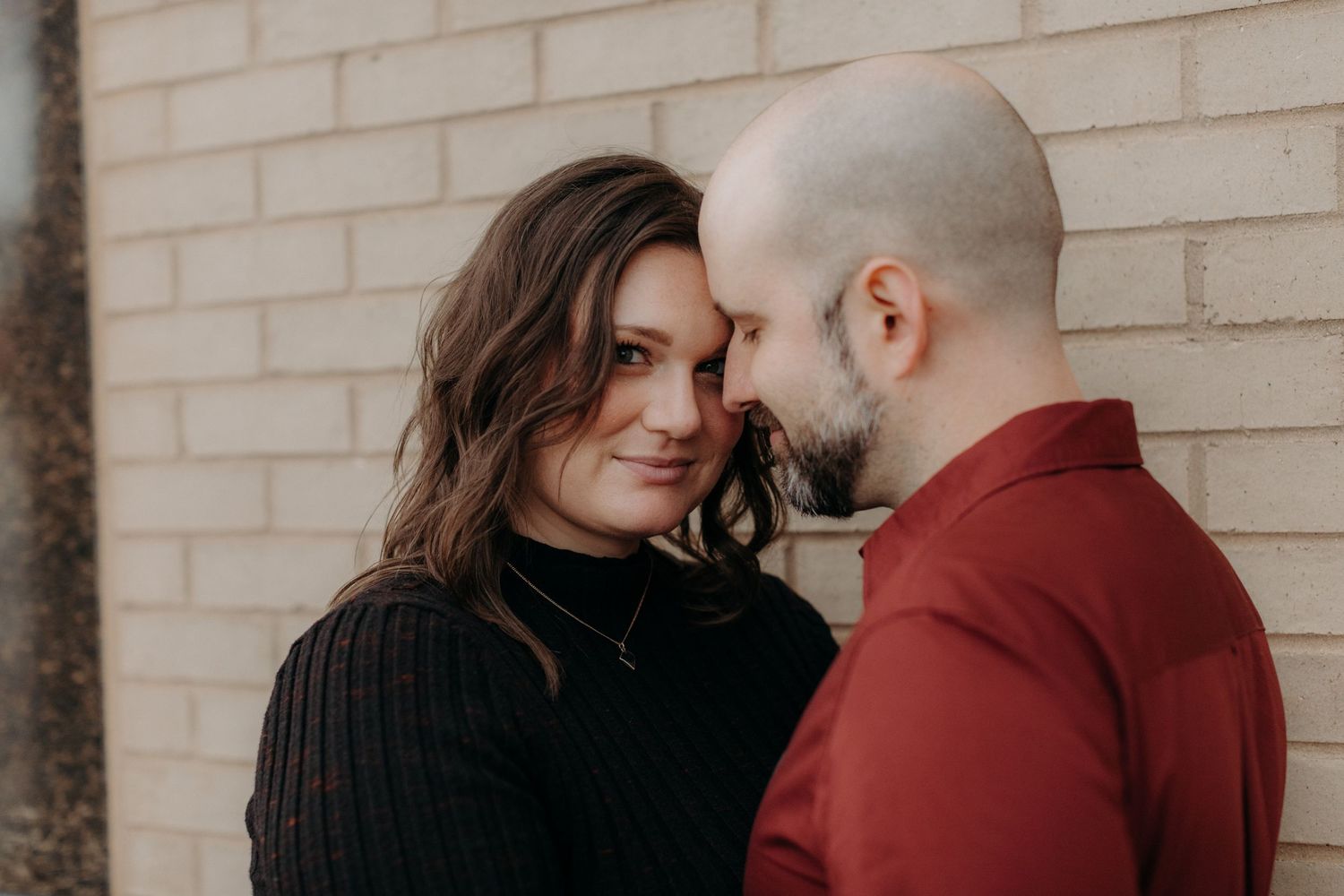 Intimate moment between couple against brick wall backdrop.
