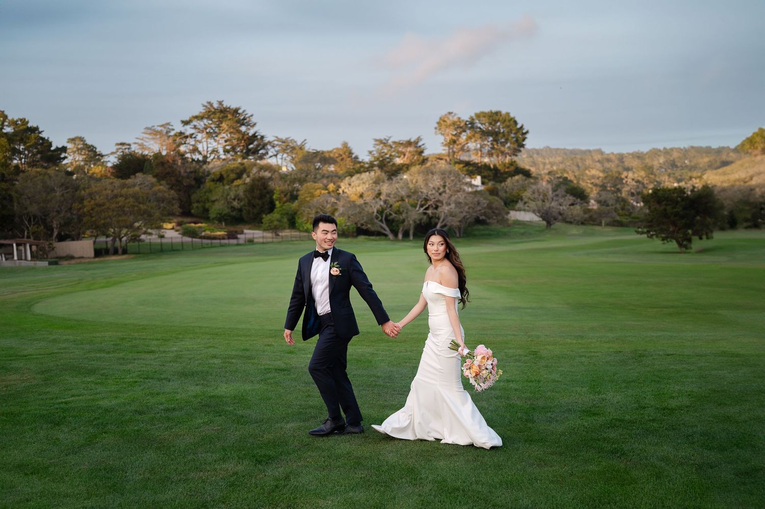 A couple celebrates their wedding day running joyfully across a scenic golf course at sunset.