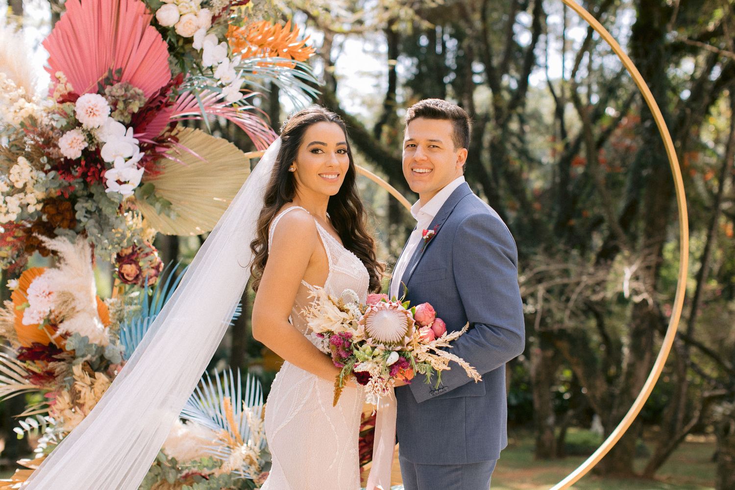 Elegant wedding arch decorated with pink flowers and palms against a natural outdoor backdrop.