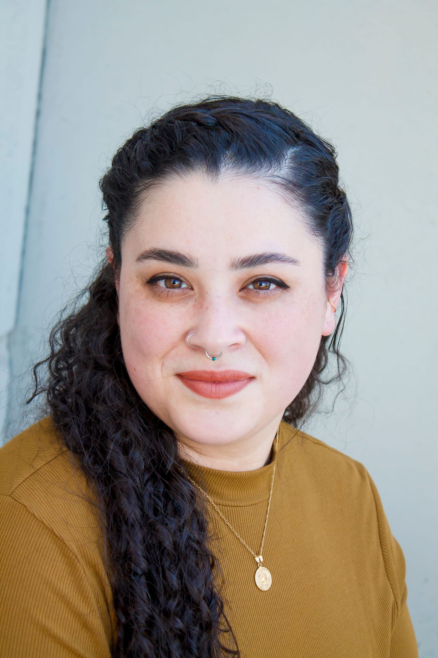 Portrait of someone in a mustard yellow sweater with long dark curly hair.